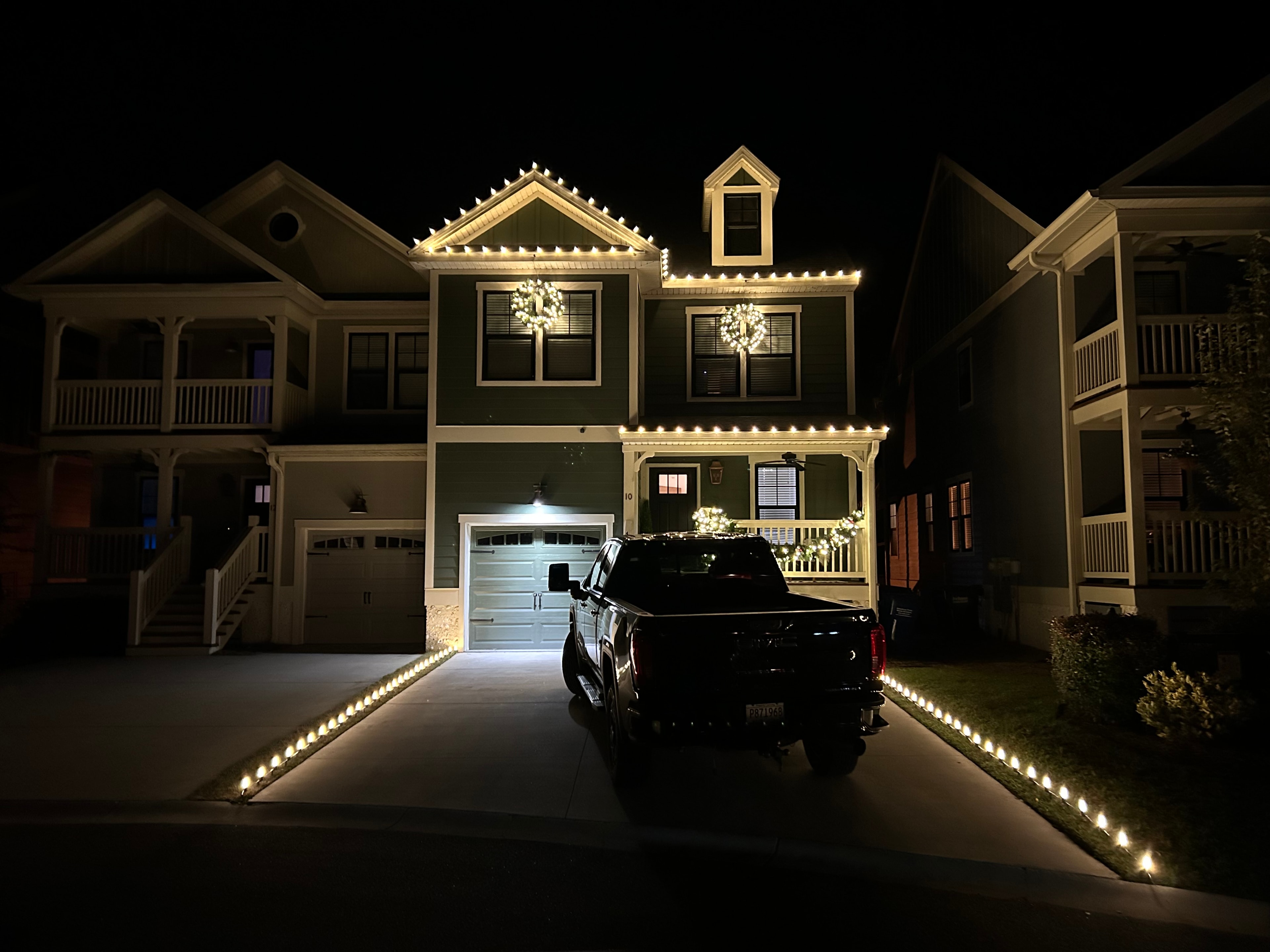 Two-story home with warm white roofline lights, lit wreaths, and driveway edge lighting