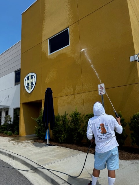 Prime Time technician pressure washing a yellow commercial building facade