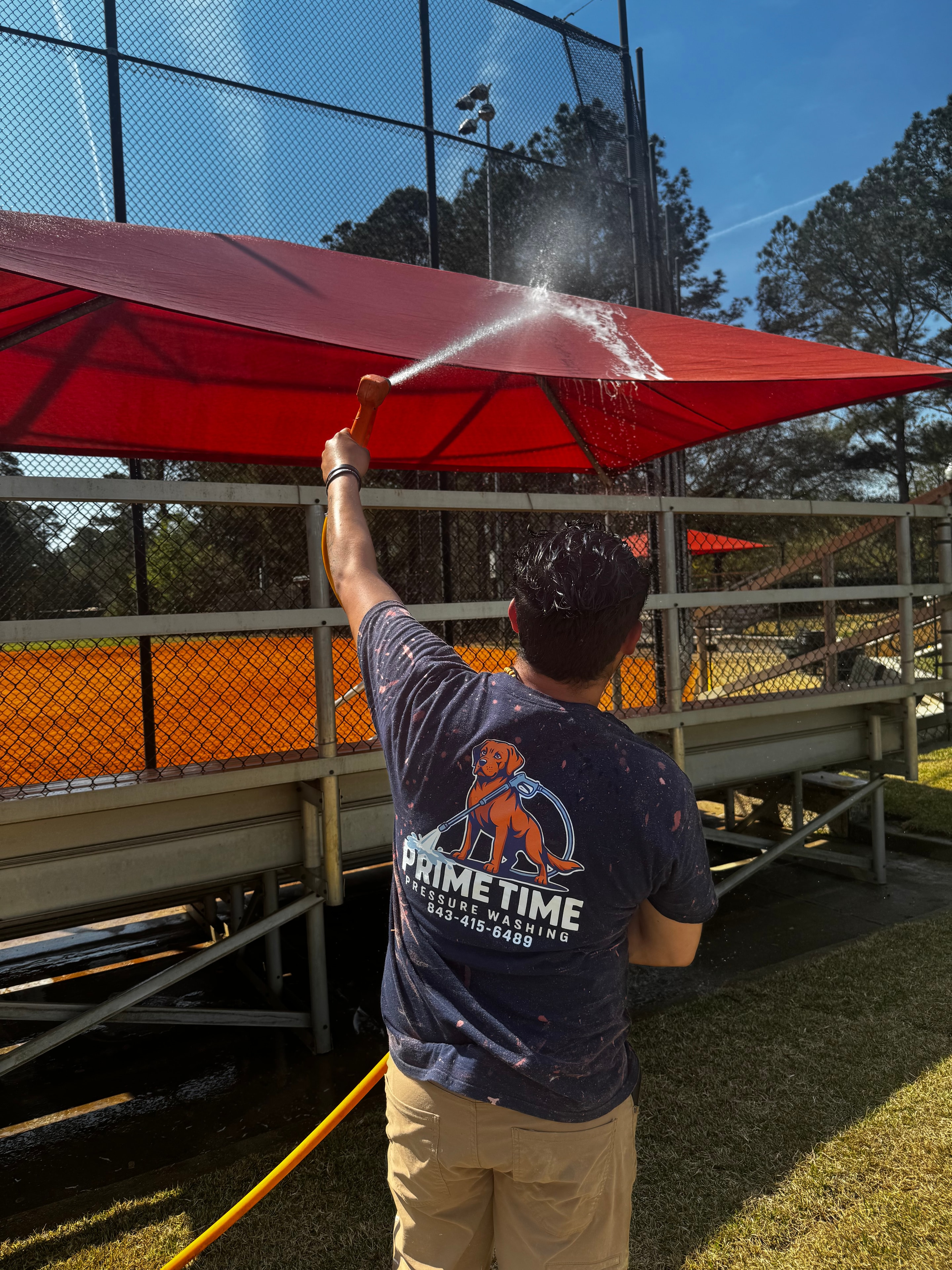 Prime Time technician pressure washing a red surface at a commercial job site